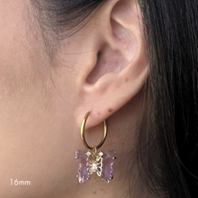 Load image into Gallery viewer, Gold hoop earring with a glass lavender butterfly charm worn by a person.