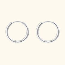 Load image into Gallery viewer, silver-colored huggie hoop earrings on a light yellow background.