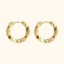Load image into Gallery viewer, Gold-colored twisted hoop earrings on a light yellow background