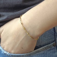 Load image into Gallery viewer, gold bracelet on a person's wrist who's wearing denim jeans and a dark gray shirt.
