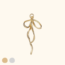 Load image into Gallery viewer, gold colored bow charm with a light yellow background.
