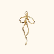 Load image into Gallery viewer, gold colored bow charm with a light yellow background.
