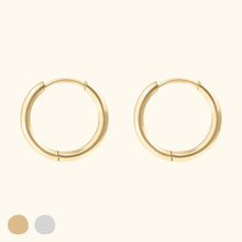 Load image into Gallery viewer, Gold-colored huggie hoop earrings on a light yellow background.
