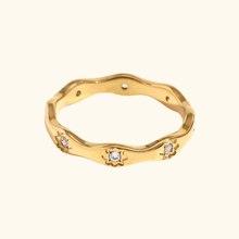 Load image into Gallery viewer, Gold-colored wavy ring with clear cubic zirconia  and starry accents on a light yellow background
