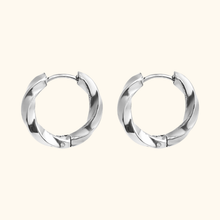Load image into Gallery viewer, Silver-colored twisted hoop earrings on a light yellow background
