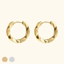 Load image into Gallery viewer, Gold-colored twisted hoop earrings on a light yellow background
